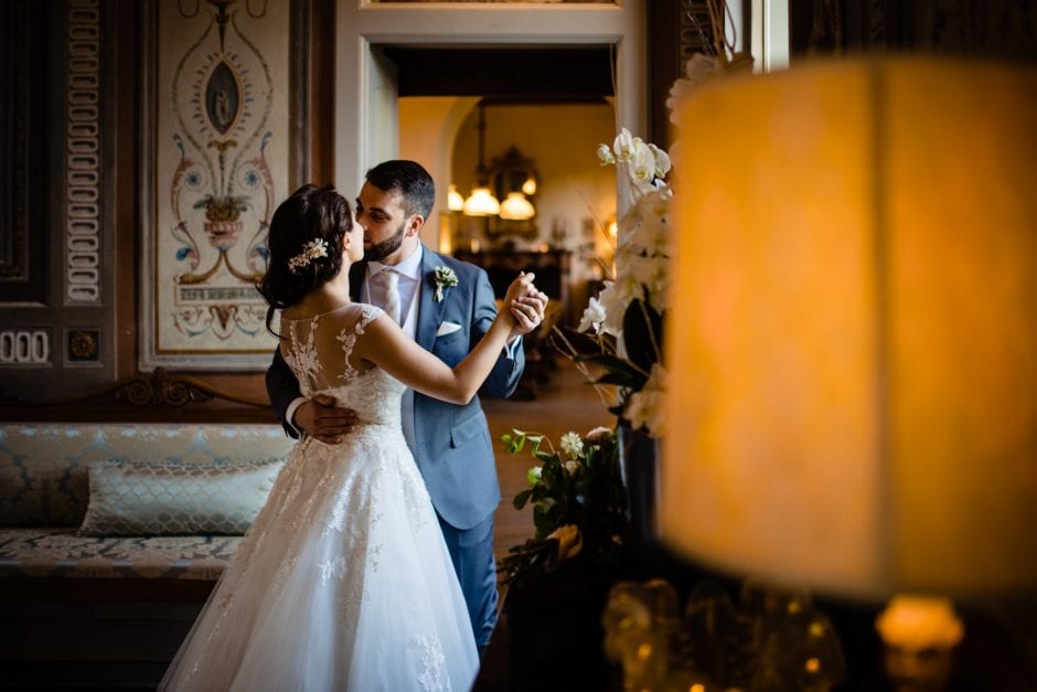Gli sposi ballano dolcemente, illuminati dalla luce calda di una finestra di Villa Bossi. fotografo matrimonio Villa Bossi