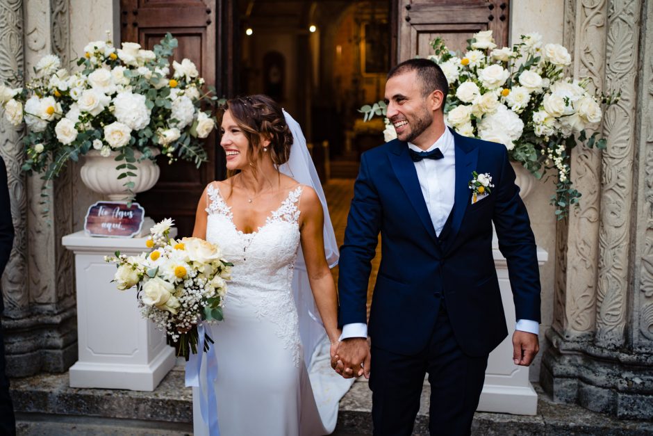 Gli sposi sorridono felici dopo il tradizionale lancio del riso all’uscita della chiesa. Fotografia scattata da Paolo Lamperti Fotografo Matrimonio Varese al Castello di Tabiano.