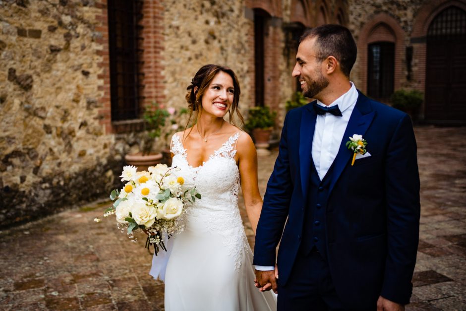 Roberta e Agustin si tengono per mano, sorridendo felici. Fotografia scattata da Paolo Lamperti Fotografo Matrimonio Varese al Castello di Tabiano.