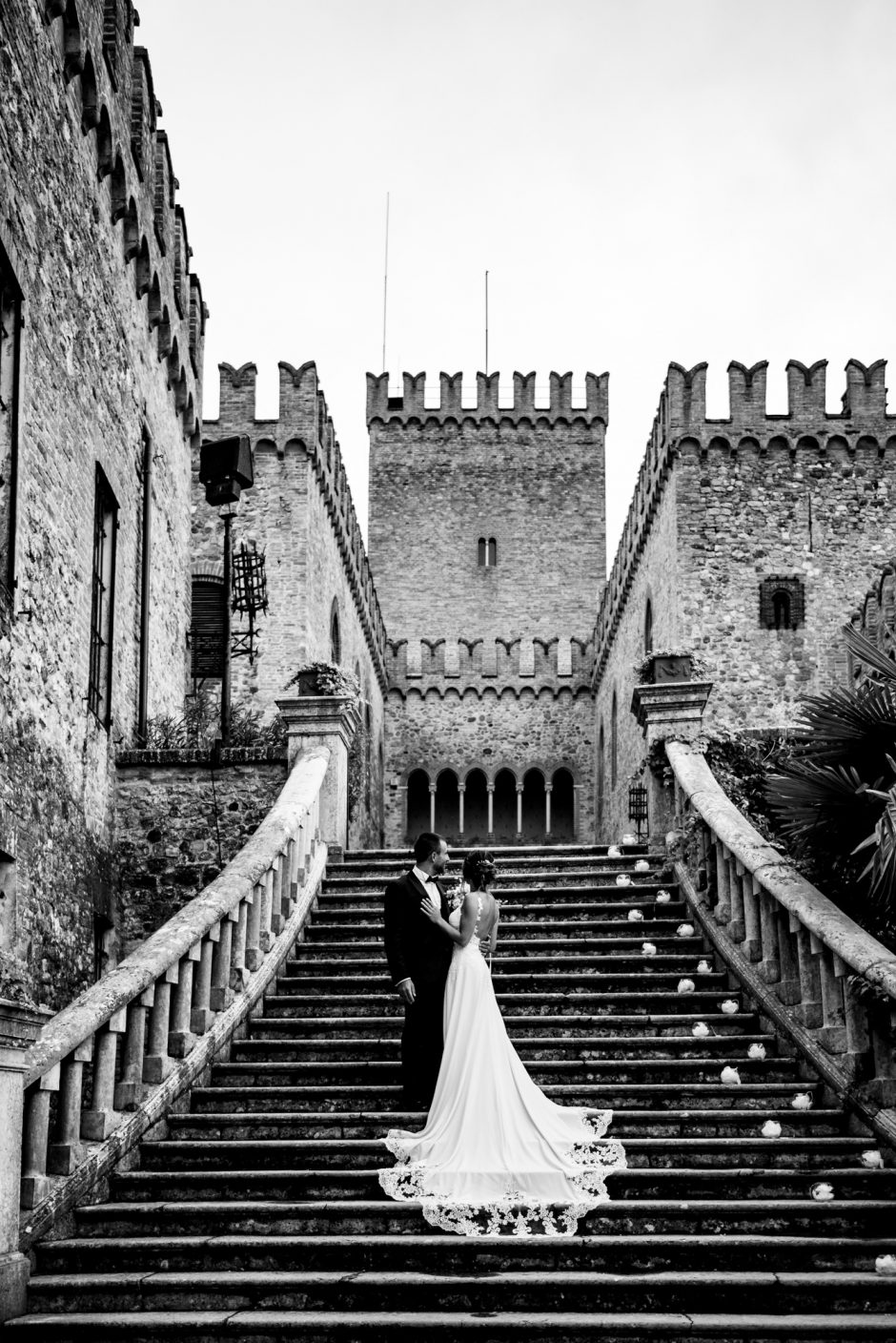 Gli sposi sulla scalinata del Castello di Tabiano, guardando la torre in uno scatto in bianco e nero. Fotografia scattata da Paolo Lamperti Fotografo Matrimonio Varese al Castello di Tabiano.